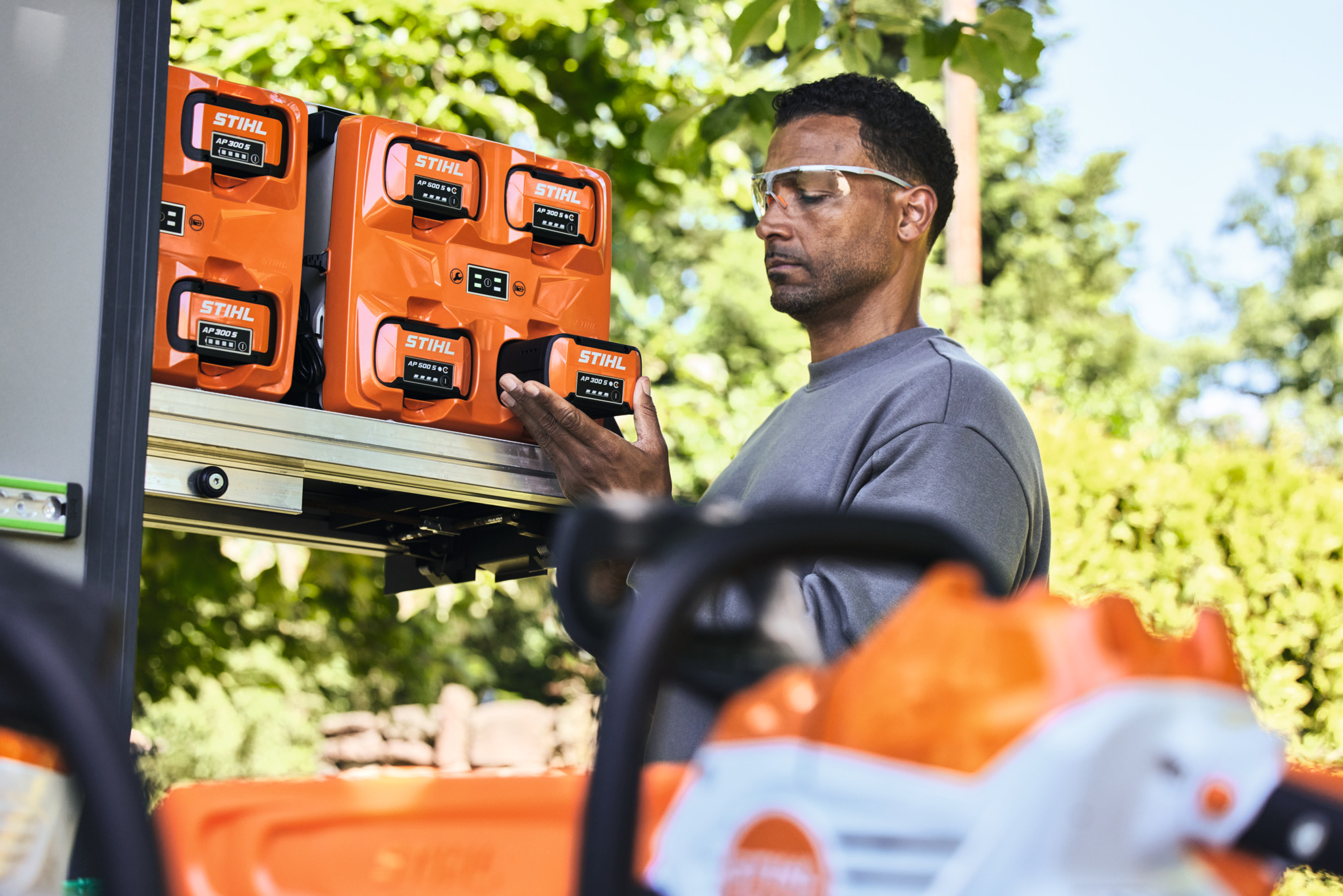 Muž v ochranných brýlích vyjímá akumulátor STIHL AP 300 S z boxu bottTainer