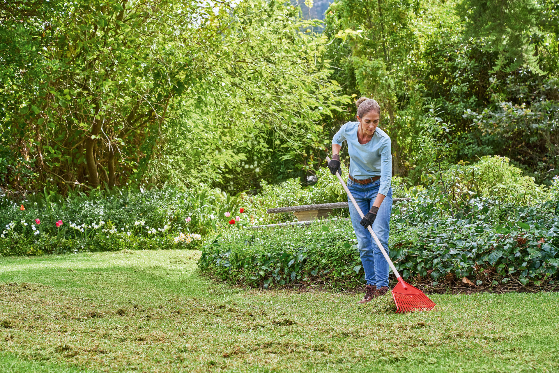 Žena provádí jarní péči o trávník a na zahradě shrabuje posečenou trávu