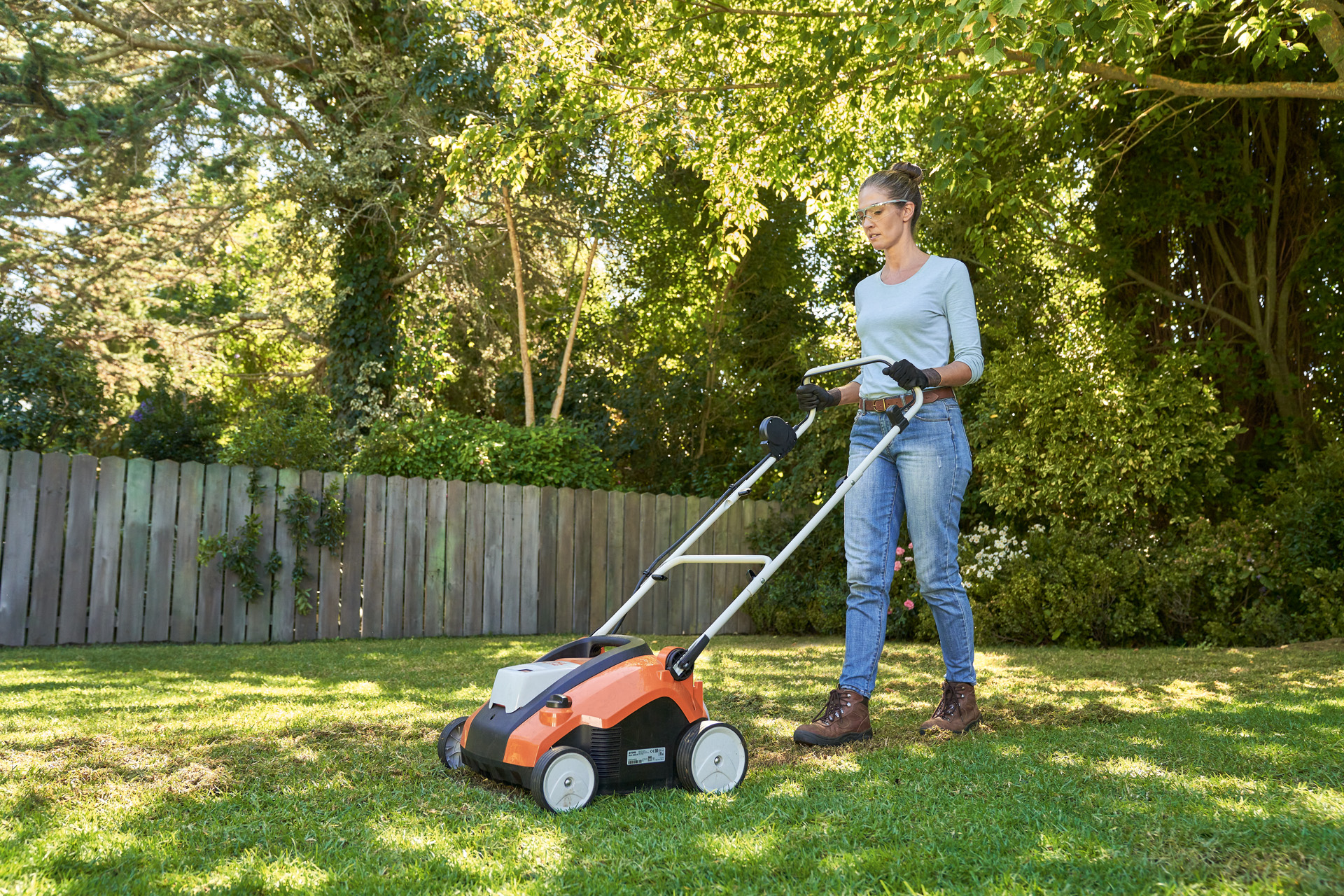Žena na zahradě provzdušňuje trávník akumulátorovým provzdušňovačem STIHL RLA 240 a je vybavena ochrannými brýlemi a pracovními rukavicemi.