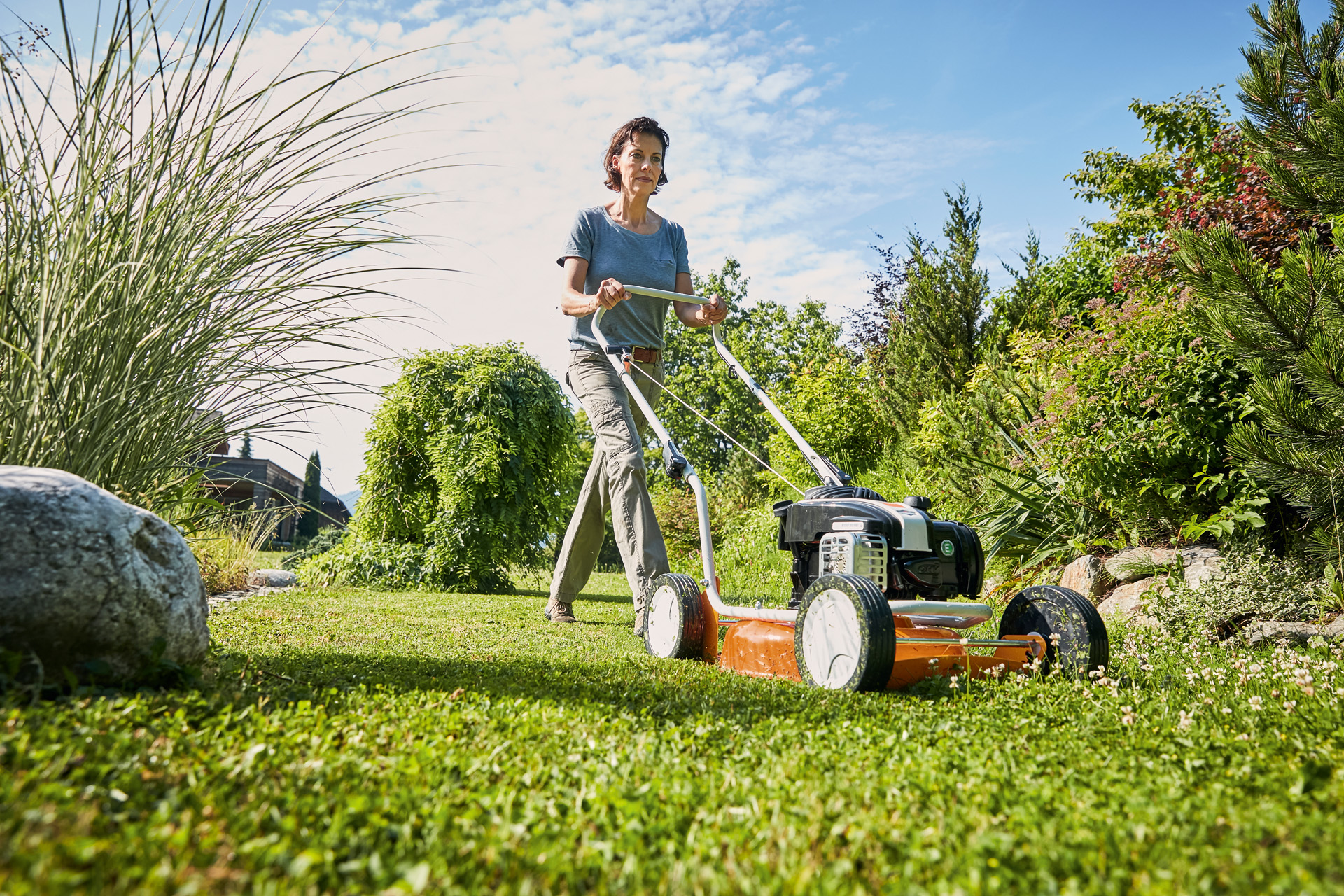 Žena používá benzínovou mulčovací sekačku STIHL RM 2 R na zelené ploše.