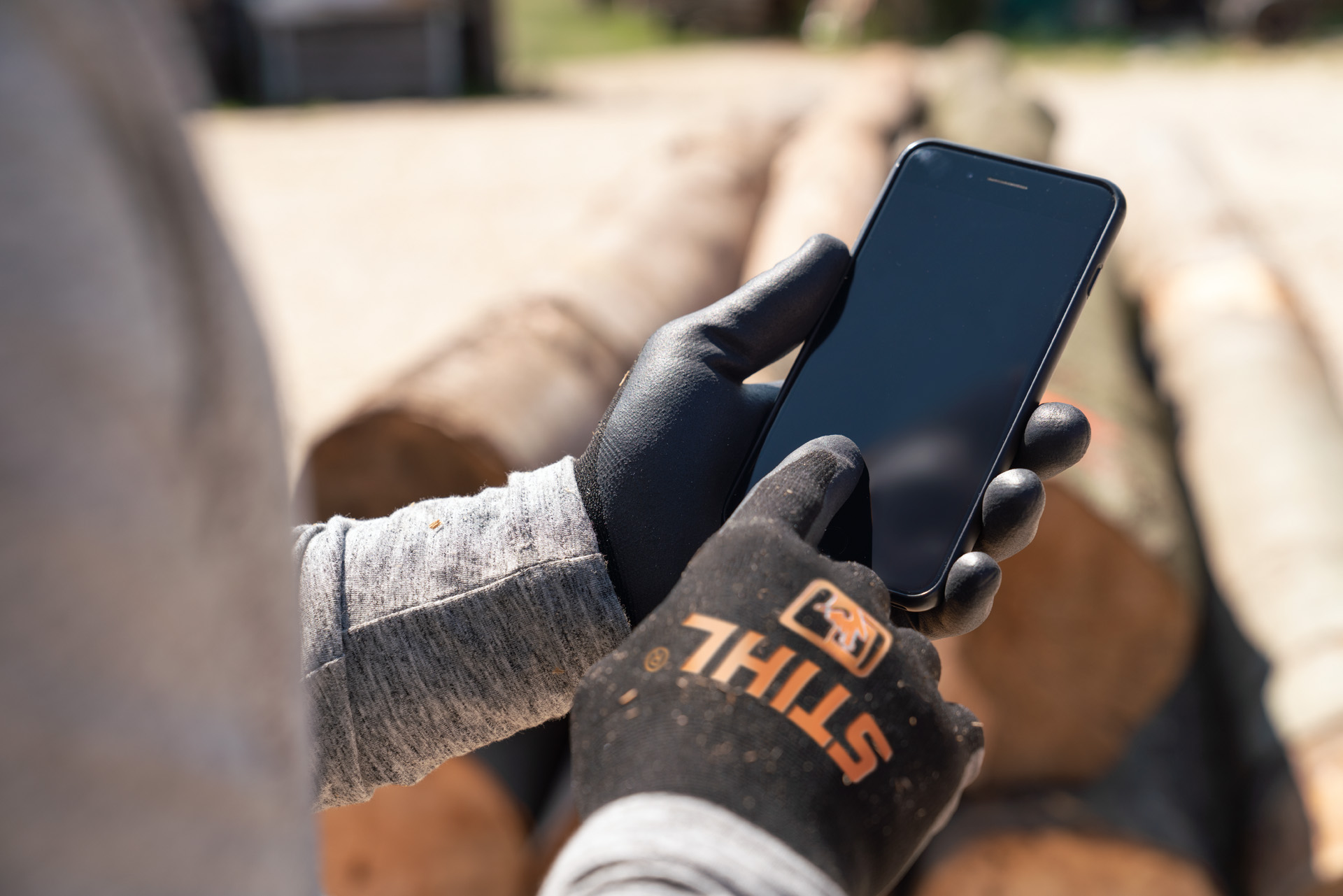 Muž v ochranných rukavicích STIHL píše na svém chytrém telefonu.