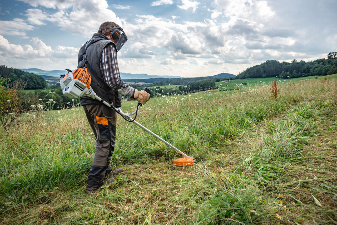 A person in protective equipment trims wildly growing undergrowth with a STIHL brush cutter