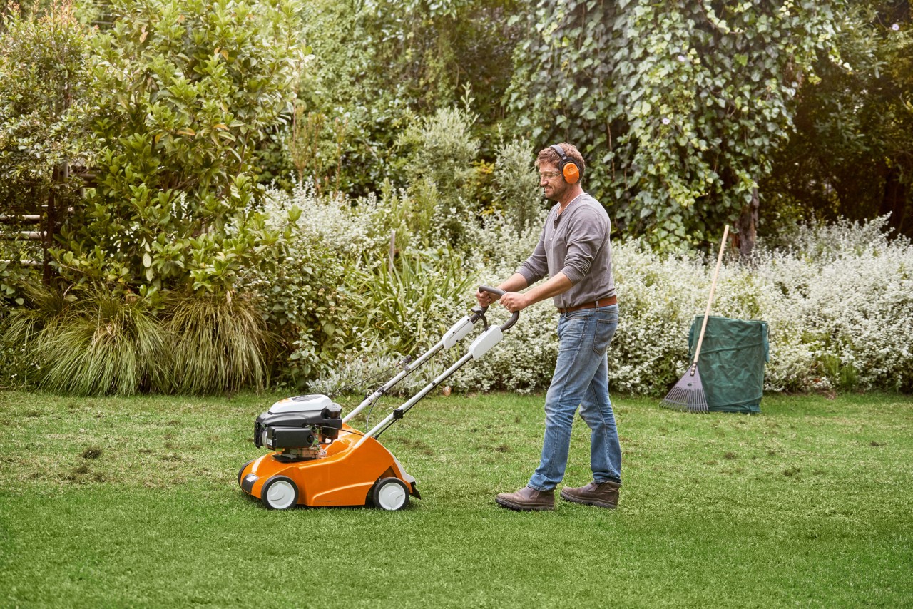 Muž provádí vertikutaci zeleného trávníku pomocí benzínového provzdušňovače STIHL RL 540