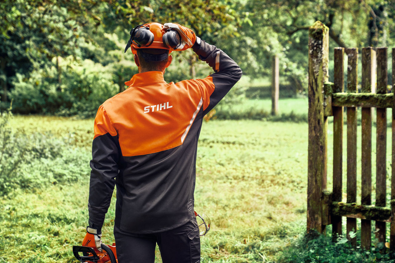 Pohled zezadu na muže v bundě STIHL FUNCTION Core s ochranou hlavy a sluchu
