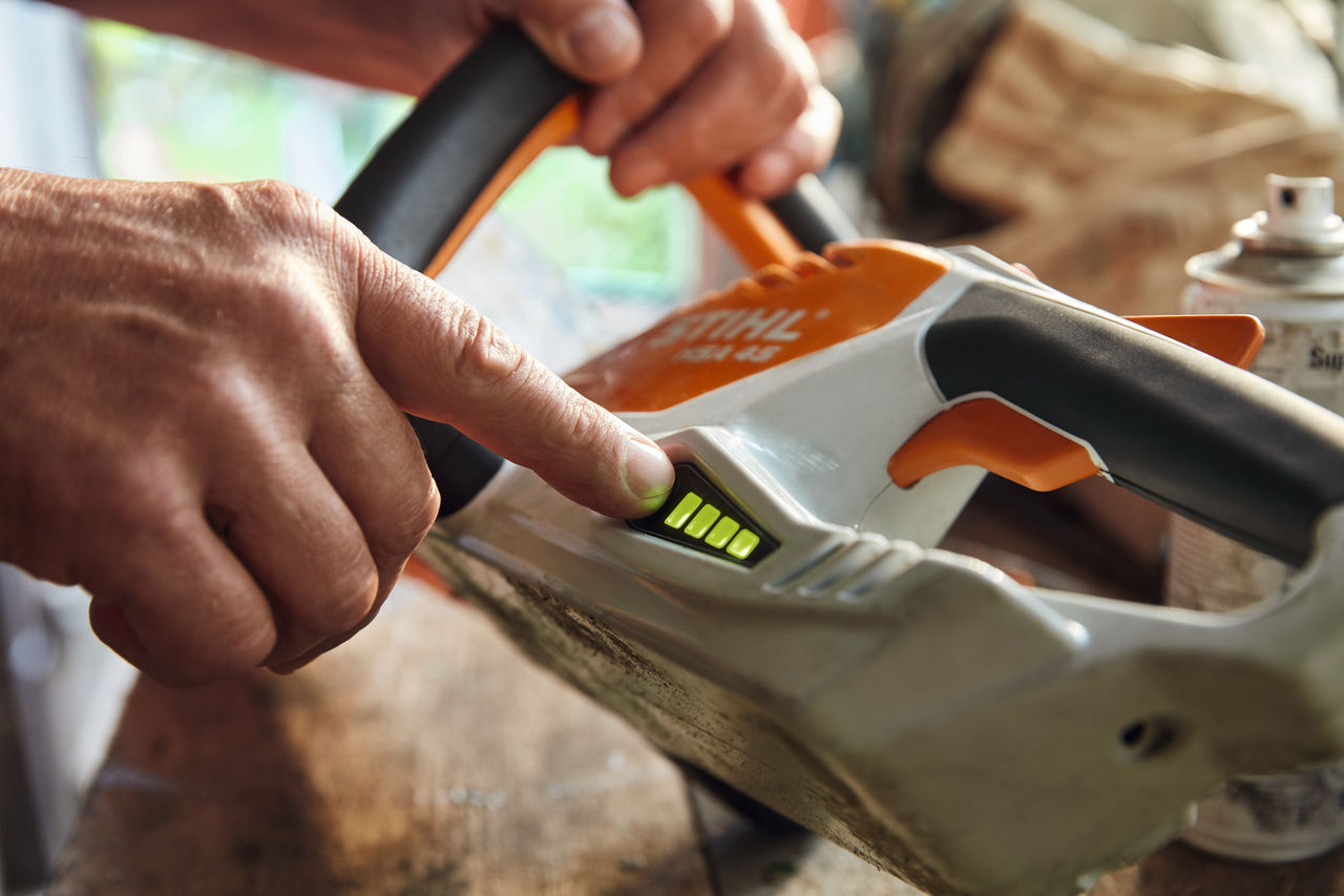 Osoba kontroluje stav nabití akumulátorových nůžek na živý plot STIHL HSA 45.