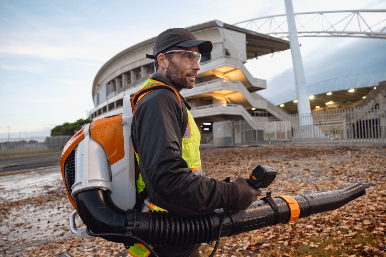 Pozdě večer člověk odklízí listí a nečistoty ze stadionu pomocí akumulátorového fukaru na listí ALLPRO STIHL BRA 600.